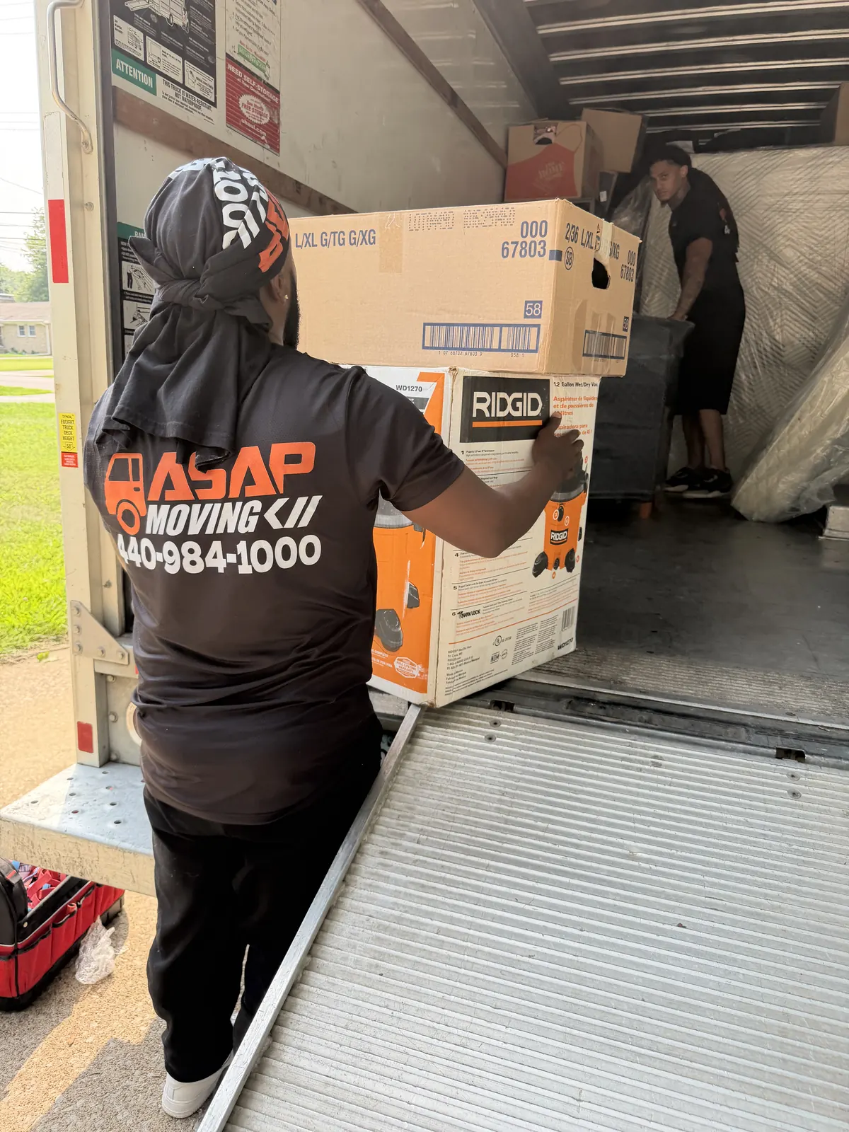 ASAP Moving crew member carrying stacked boxes beside a moving truck ramp in Amherst, Ohio.